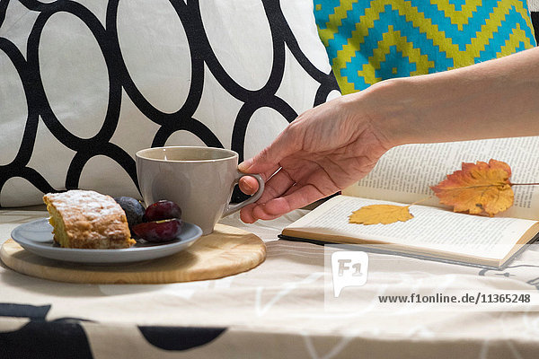 Hand einer Frau mit Tasse Kaffee und Kuchen auf dem Sofa