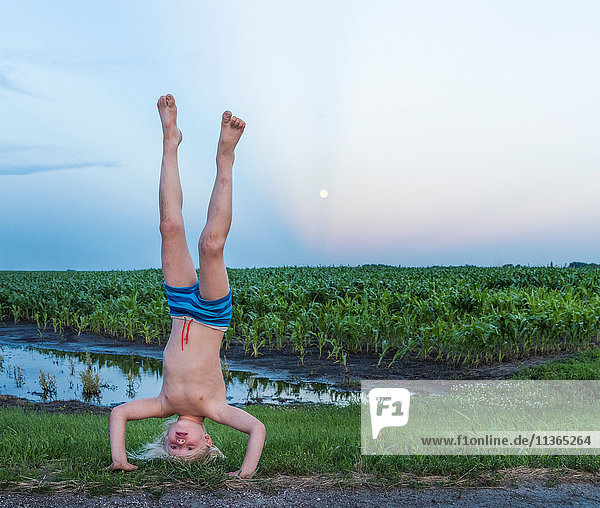 Boy wearing shorts doing handstand in rural area