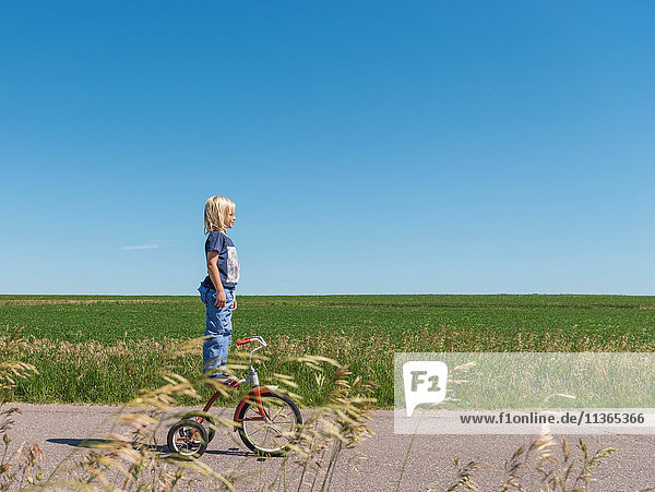 Seitenansicht eines auf einem Dreirad stehenden Jungen in ländlicher Gegend