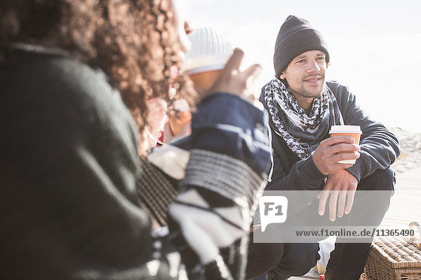 Junge erwachsene Freunde kauern am Strand mit Kaffee zum Mitnehmen  Western Cape  Südafrika