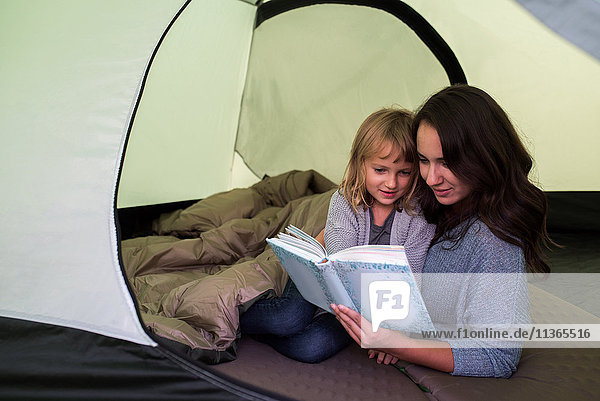 Mutter und Tochter im Schlafsack im Zelt  gemeinsam Buch lesen