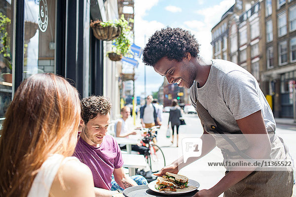 Kellner serviert Mittagessen zu Paar in der Stadt Bürgersteig Cafe
