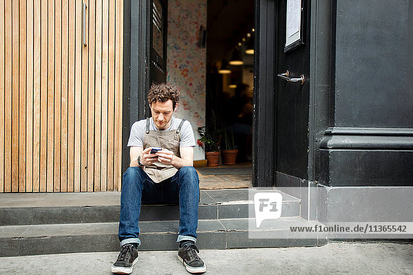 Waiter taking a break on cafe step looking at smartphone