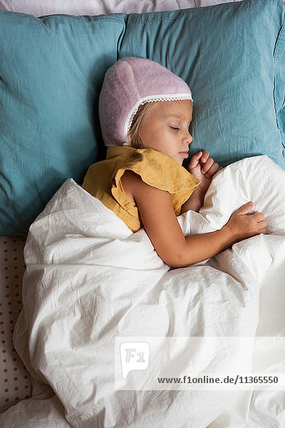 Junges Mädchen schläft im Bett und trägt einen warmen Hut