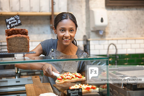 Waitress serving open sandwich from cafe display cabinet