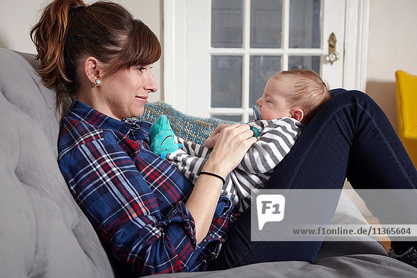 Mother sitting on sofa looking at sleeping baby boy  smiling