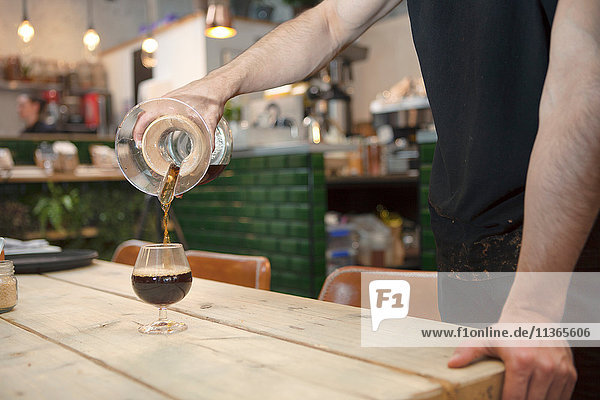 Männliche Barista's Hände gießen schwarzen Kaffee in Brandy-Glas im Cafe