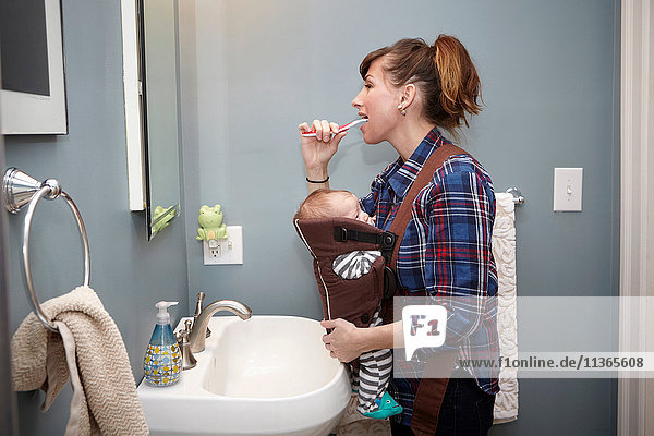 Mother with baby boy in baby sling  brushing teeth