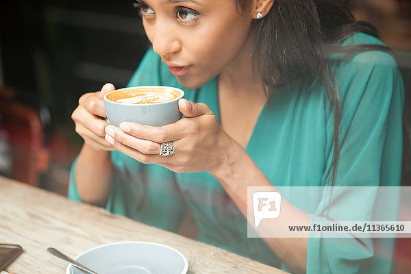 Mittlere erwachsene Frau  die eine Kaffeetasse hält und aus dem Café-Fenster schaut