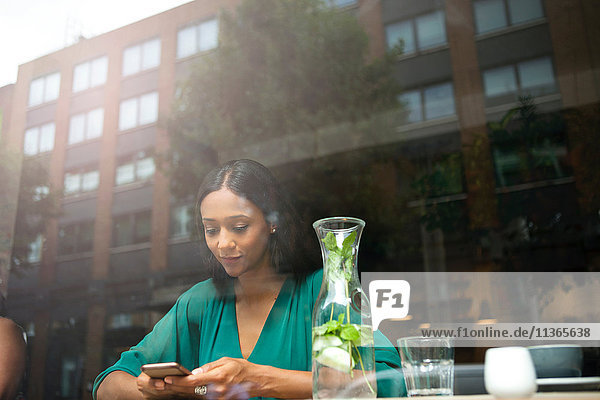 Mittlere erwachsene Frau beim Lesen von Smartphone-Texten im Café-Fenstersitz
