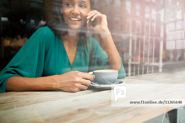 Mittlere erwachsene Frau beim Plaudern auf dem Smartphone im Café-Fenstersitz