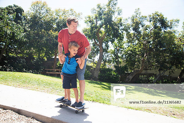 Vater und Sohn üben im Park auf dem Skateboard