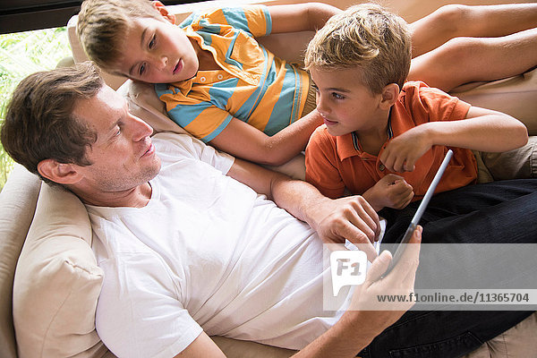 Mann und zwei Söhne benutzen digitalen Tablet-Touchscreen auf dem Sofa