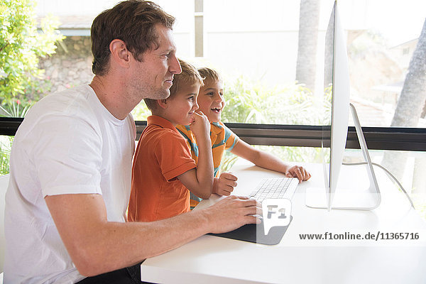 Man and two sons using desktop computer