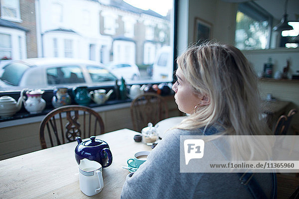 Junge Frau im Café sitzend  Tasse Tee und Teekanne auf dem Tisch  Blick aus dem Fenster