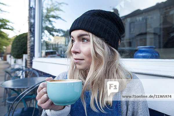 Junge Frau sitzt vor dem Café und trinkt eine Tasse Tee.