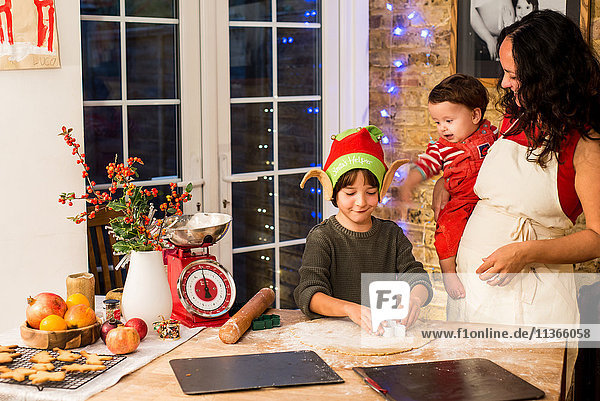 Reife Frau bereitet mit Söhnen an der Küchentheke Weihnachtsplätzchen zu