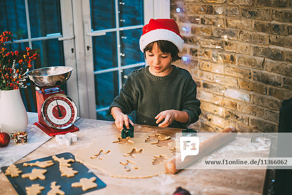 Junge mit Weihnachtsmannhut bereitet Weihnachtsplätzchen an der Küchentheke zu