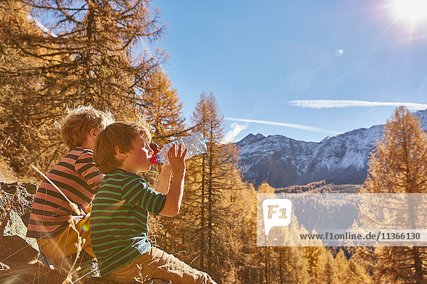 Zwei Jungen sitzen auf Felsen und trinken aus Wasserflaschen  Schnalstal  Südtirol  Italien