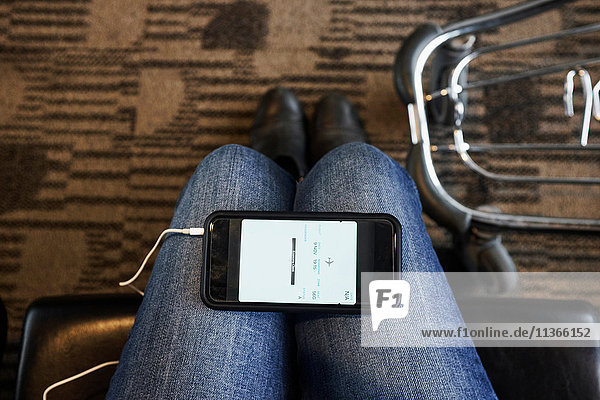 Persönliche Perspektive eines Smartphones auf den Knien der Frau in der Flughafen-Lounge