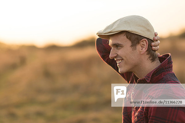 Junger Mann in ländlicher Umgebung  lächelnd  Seitenansicht