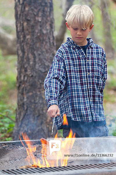 Boy barbecuing sausage on flaming grill in forest  Sedona  Arizona  USA