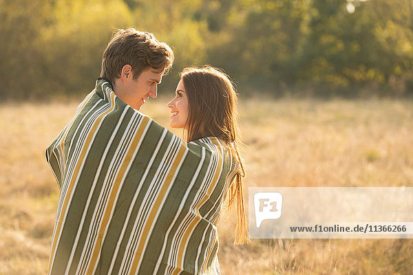 Junges Paar in ländlicher Umgebung  in eine Decke gewickelt  von Angesicht zu Angesicht  lächelnd