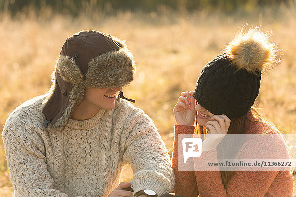 Junges Paar sitzt in ländlicher Umgebung und trägt warme Hüte