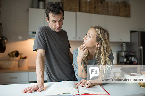 Mittleres erwachsenes Paar liest Rezeptbuch in der Küche