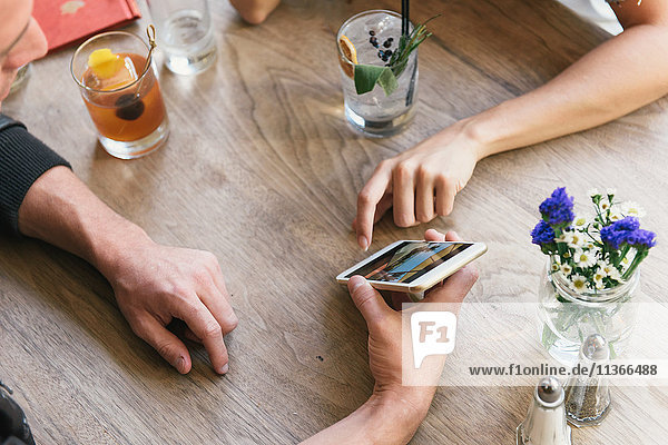 Junges Paar zeigt am Cocktail-Bar-Tisch auf ein Smartphone