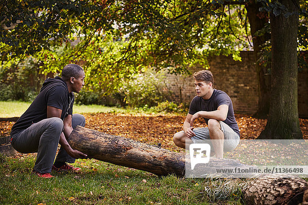 Personal Trainer zeigt jungen Mann  wie man Baumstämme im Park hebt.