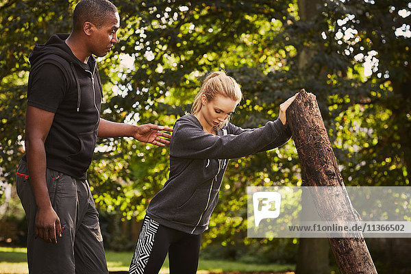 Junge Frau mit Personal Trainerin beim Baumstammheben im Park