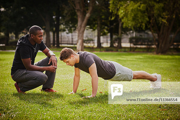 Personal Trainerin  die den jungen Mann bei Push-ups im Park unterweist.