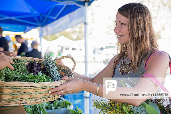 Frau am Obst- und Gemüsestand erhält Korb mit frischen Kräutern