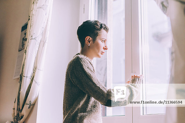 Porträt einer jungen Frau  die zu Hause durchs Fenster starrt.
