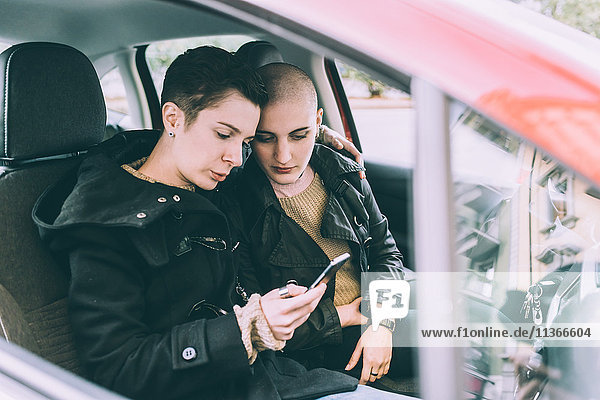 Junges lesbisches Paar sitzt im Auto und liest Smartphone-Texte