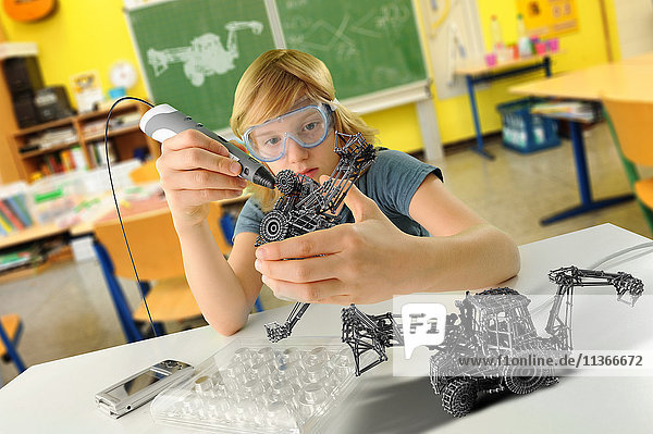 Junge mit digitalem Stift und 3D-Modell eines Baggers im Klassenzimmer