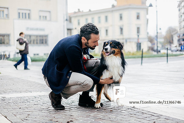 Mid adult man crouching to pet dog in cobbled city square