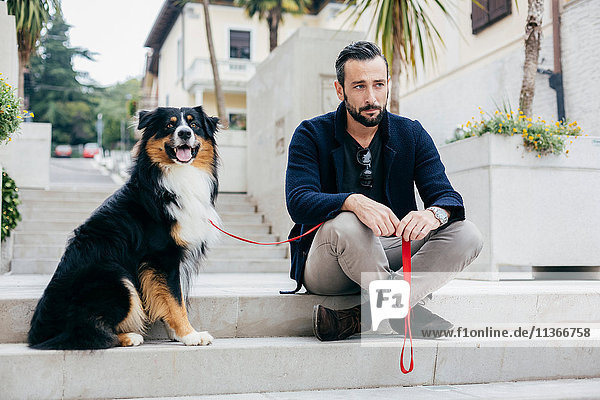 Mittelgroßer erwachsener Mann sitzt auf einer Treppe mit einem Hund auf dem Stadtplatz