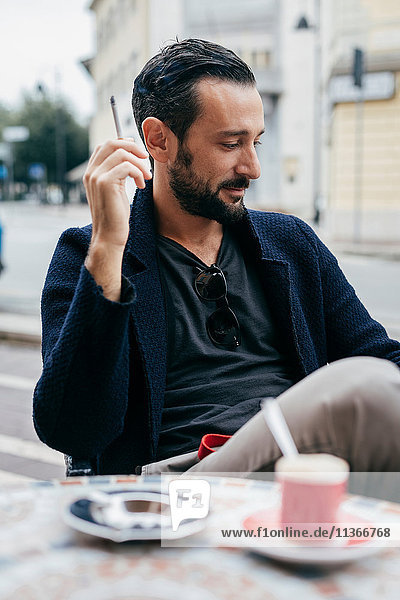 Mittelgroßer erwachsener Mann raucht Zigarette im Straßencafé