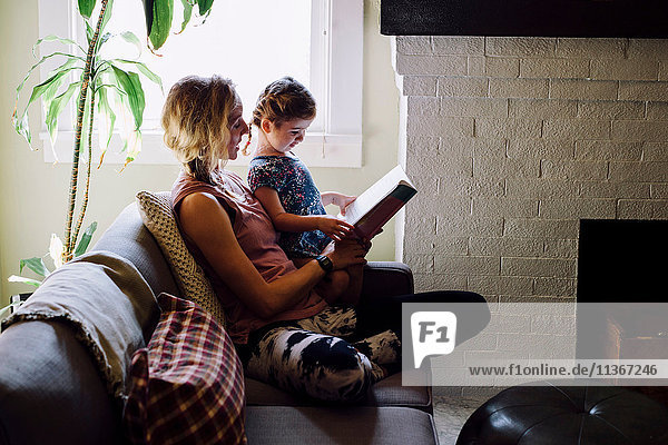 Woman on sofa with toddler daughter reading storybook