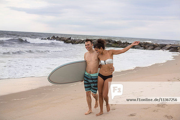 Romantic young surfing couple strolling on Rockaway Beach  New York State  USA