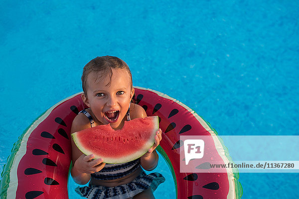 Junges Mädchen im Schwimmbad  entspannt auf aufblasbarem Ring  isst Wassermelone