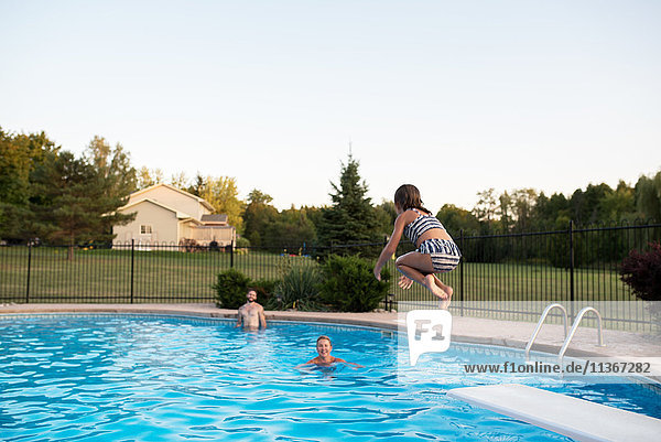 Junges Mädchen springt ins Schwimmbad  Vater und Großmutter schauen zu