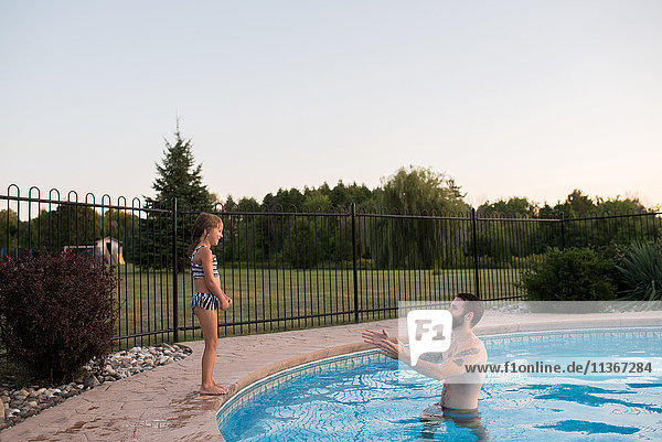 Junges Mädchen steht am Rand eines Swimmingpools  der Vater im Pool ermutigt sie  hineinzuspringen