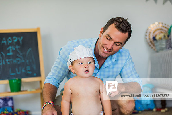 Father smiling at toddler wearing funny hat