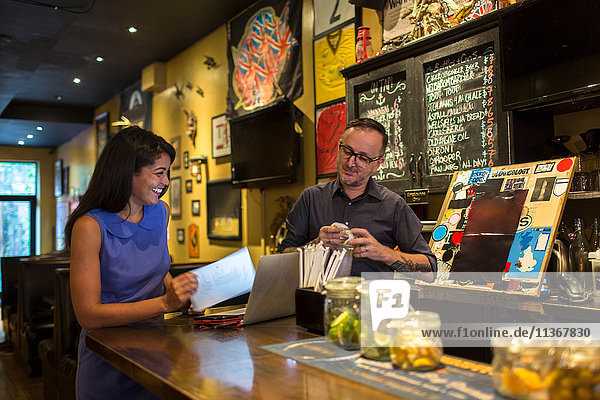 Barman laughing with female customer at public house counter