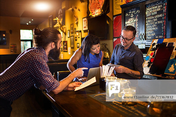 Barman reading menu with young couple at public house counter