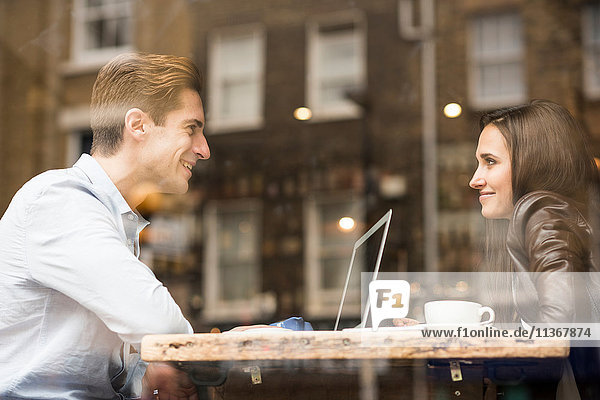 Young businessman and woman with laptop talking in cafe