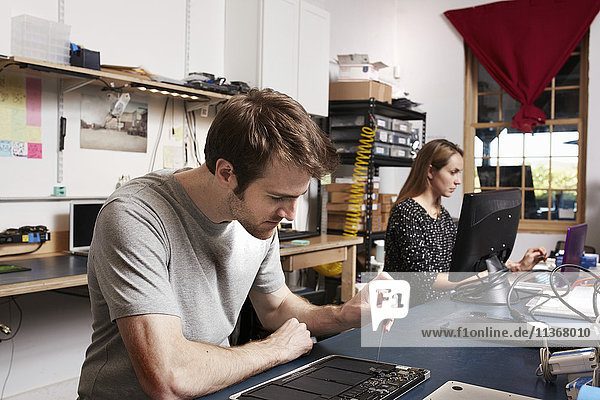 A young man and woman working at a bench in a technology lab.